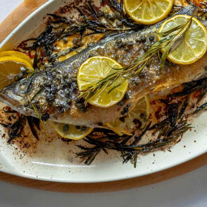 A Branzino on a plate with lemon slices and rosemary.