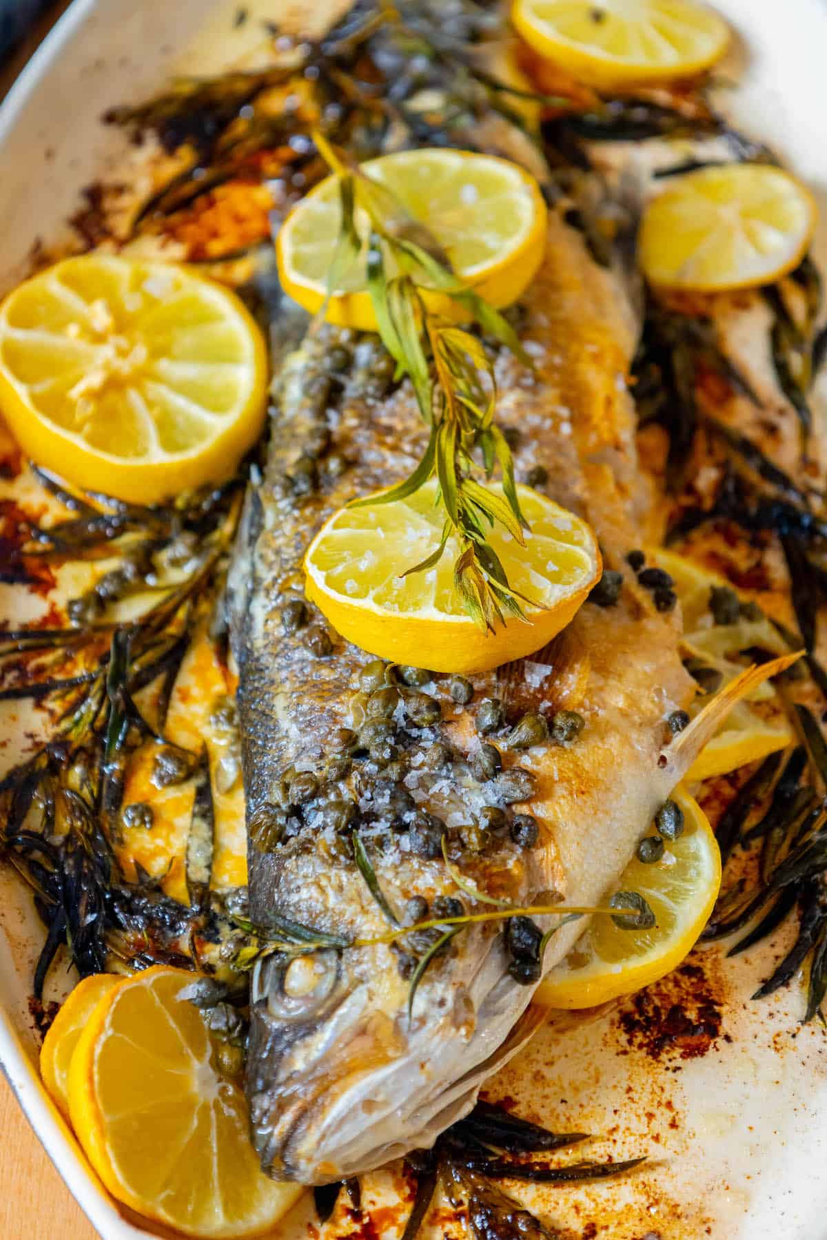 A roasted Branzino served with lemon slices and herbs on a plate.