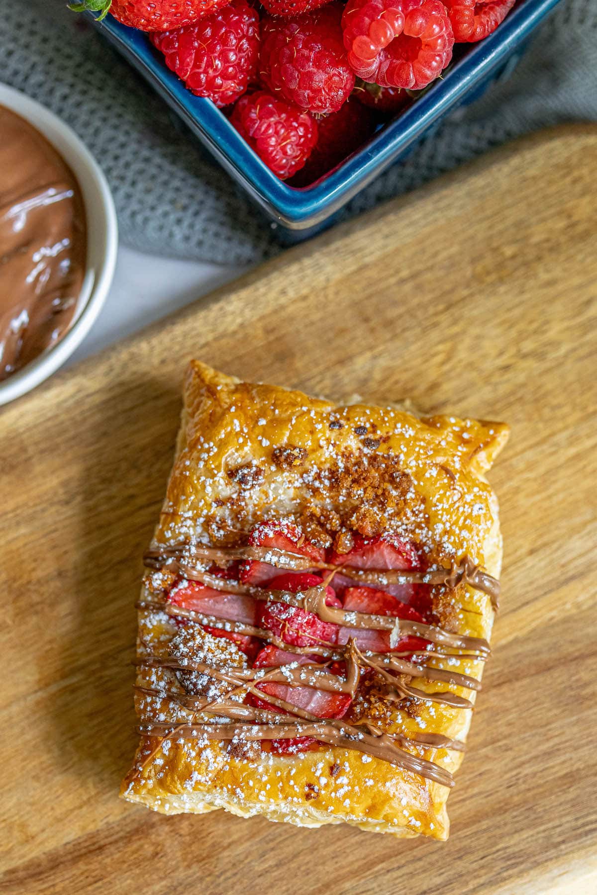 baked fruit tart on a table with berries and drizzled nutella on top