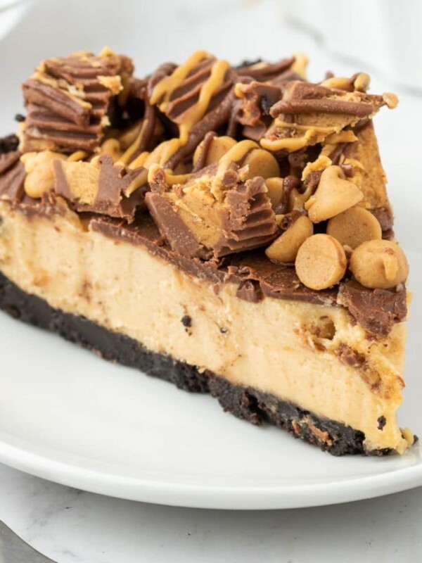 a slice of peanut butter pie on a white plate topped with peanut butter chips and peanut butter cups