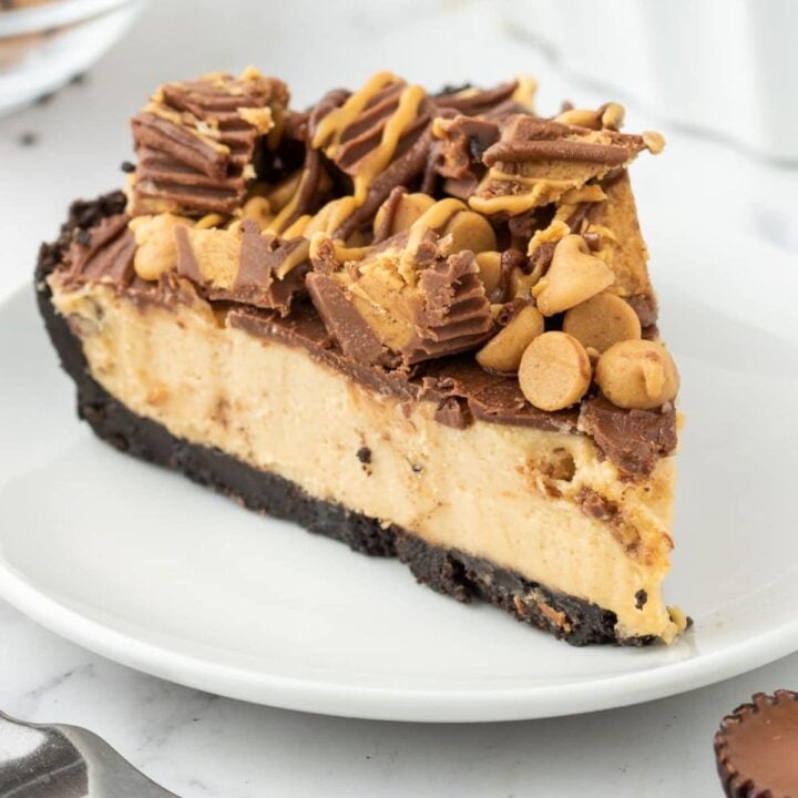 a slice of peanut butter pie on a white plate topped with peanut butter chips and peanut butter cups