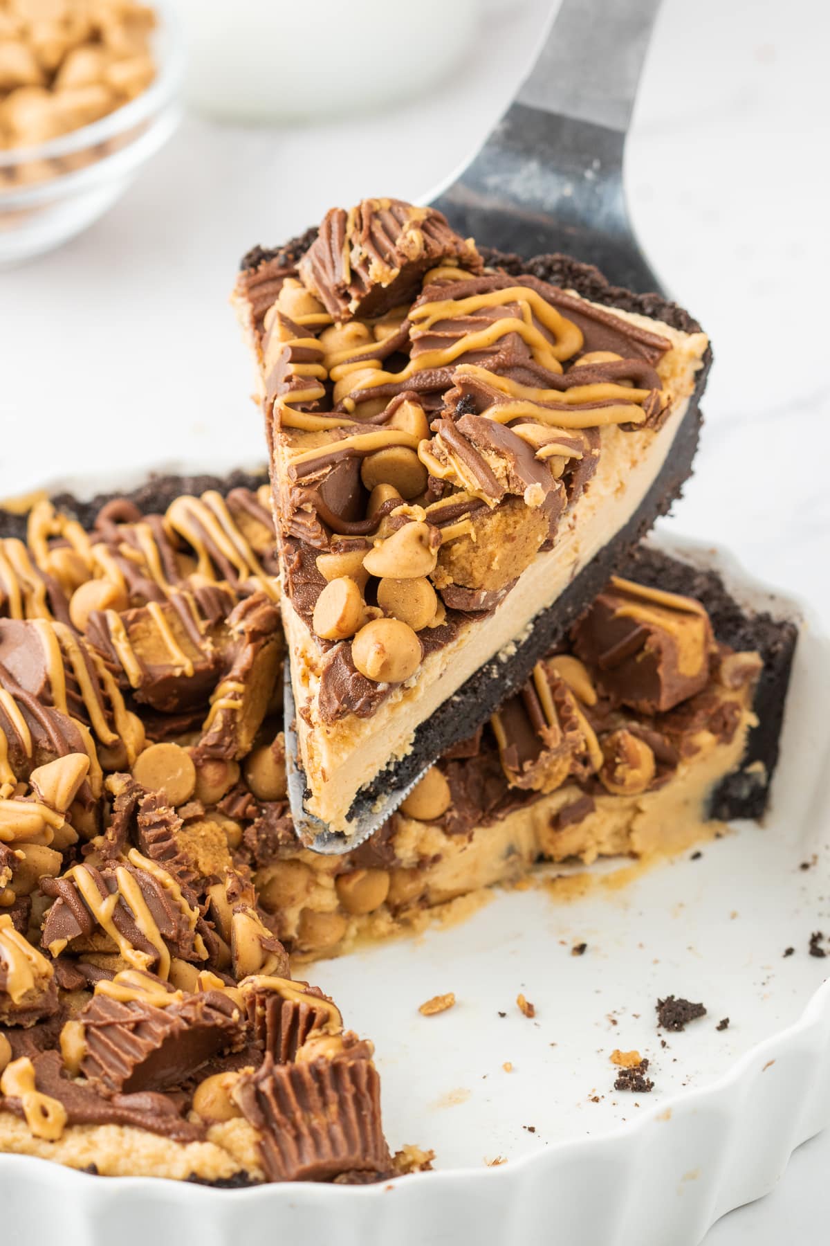 piece of pie with peanut butter cups on it and butterscotch chips, creamy filling, chocolate crust being cut out of a larger pie