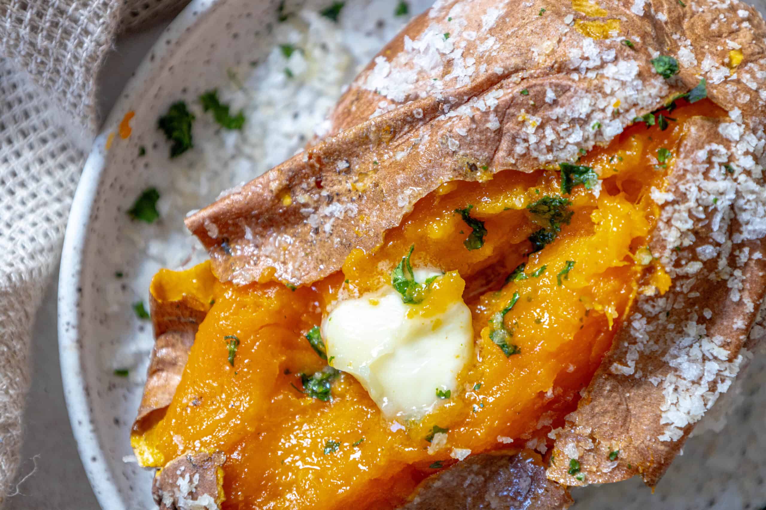 A salt baked sweet potato with butter and parsley on a plate.