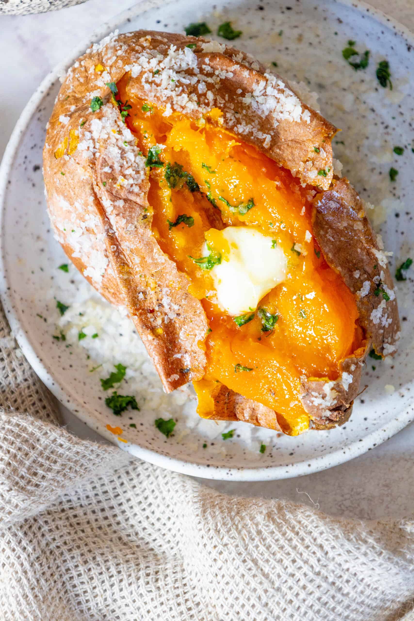 A Salt Baked Sweet Potato with butter and parsley on a plate.