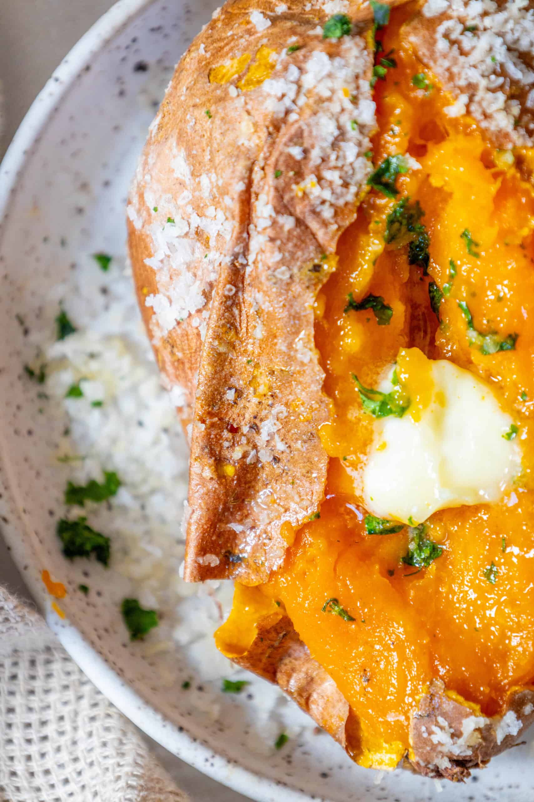 A salt-baked sweet potato with butter and parsley on a plate.