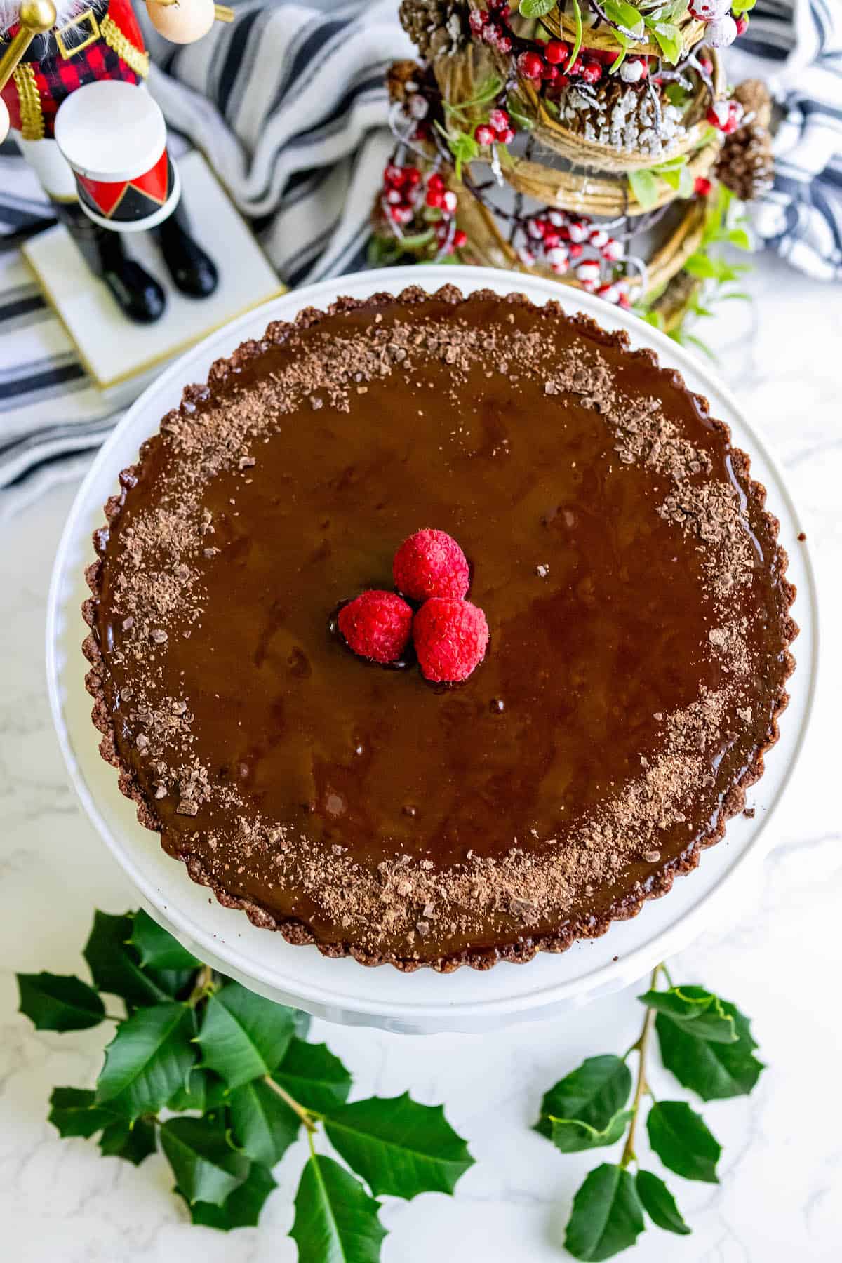 A silky chocolate tart topped with raspberries on a white plate.