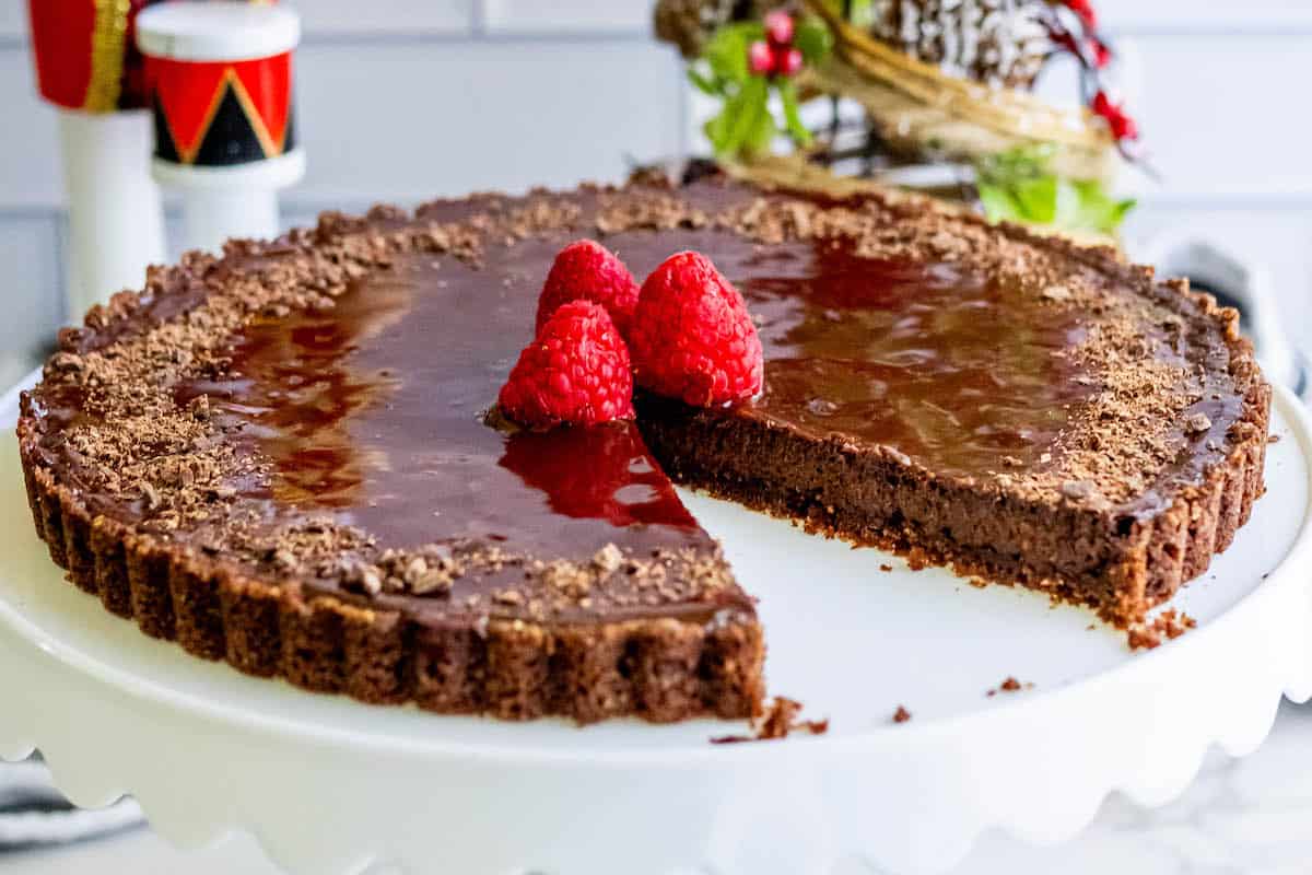A silky chocolate tart with raspberries on a white plate.