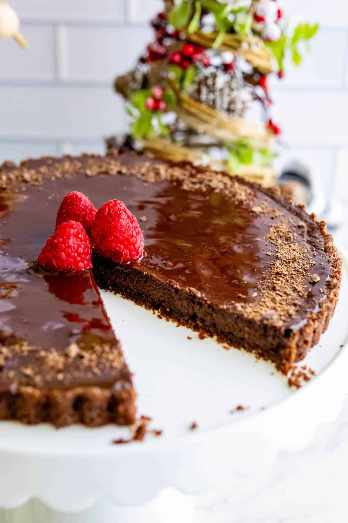 A silky chocolate tart garnished with raspberries on a white plate.