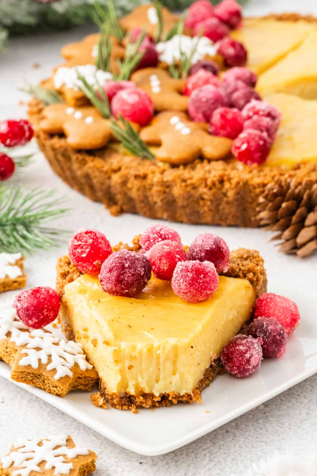 A slice of eggnog tart with cranberries and gingerbread cookies on a plate.