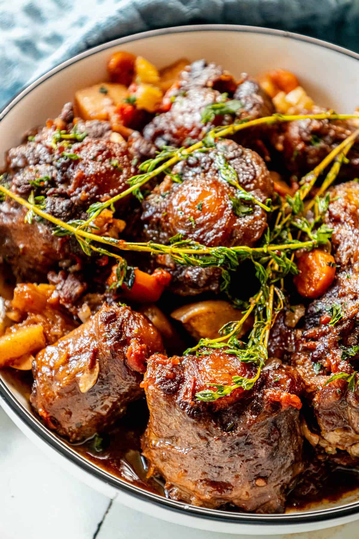 A bowl of roasted oxtail stew with carrots and sprigs of thyme.