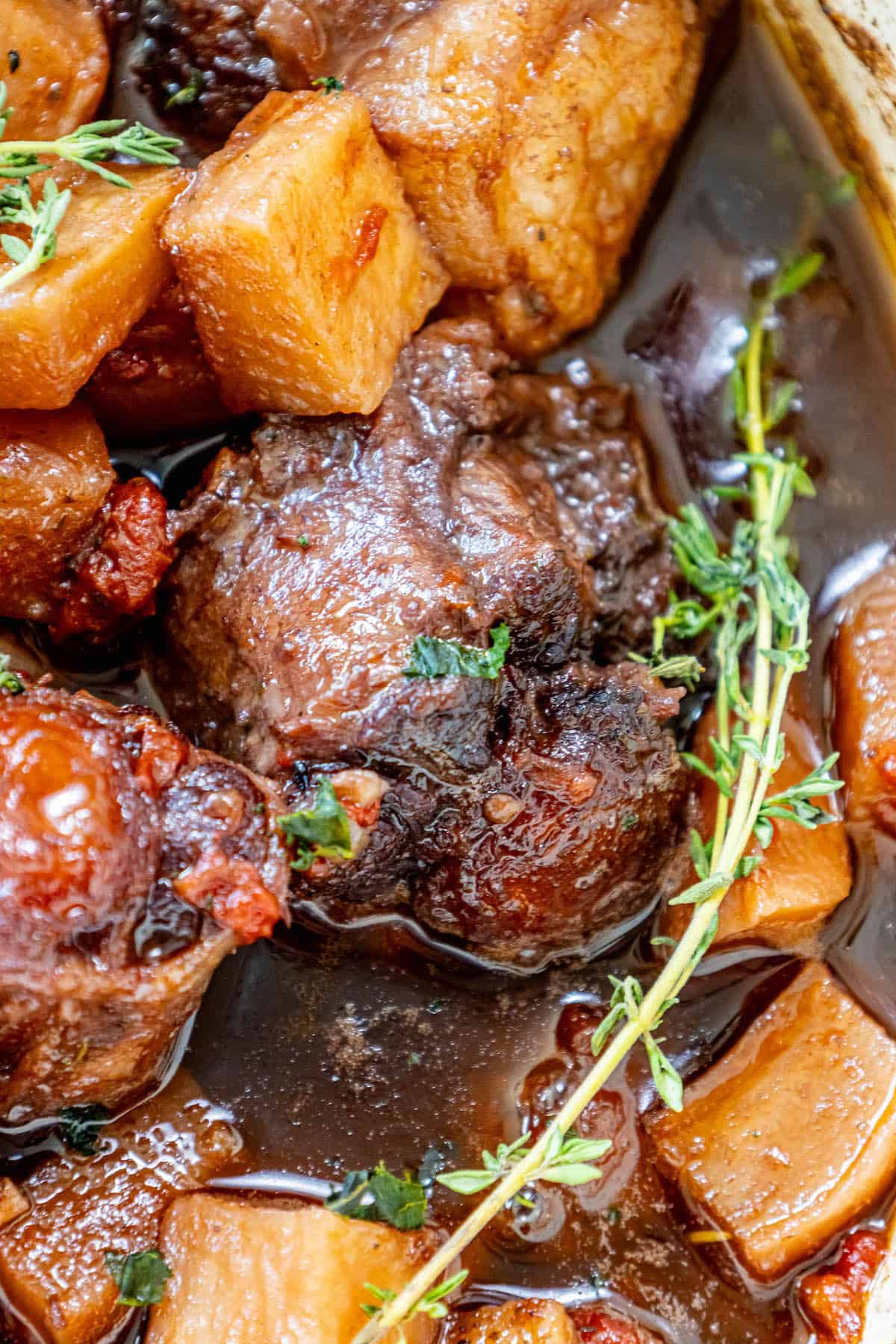 A Roasted Oxtail Stew with meat, potatoes, and sprigs of thyme.