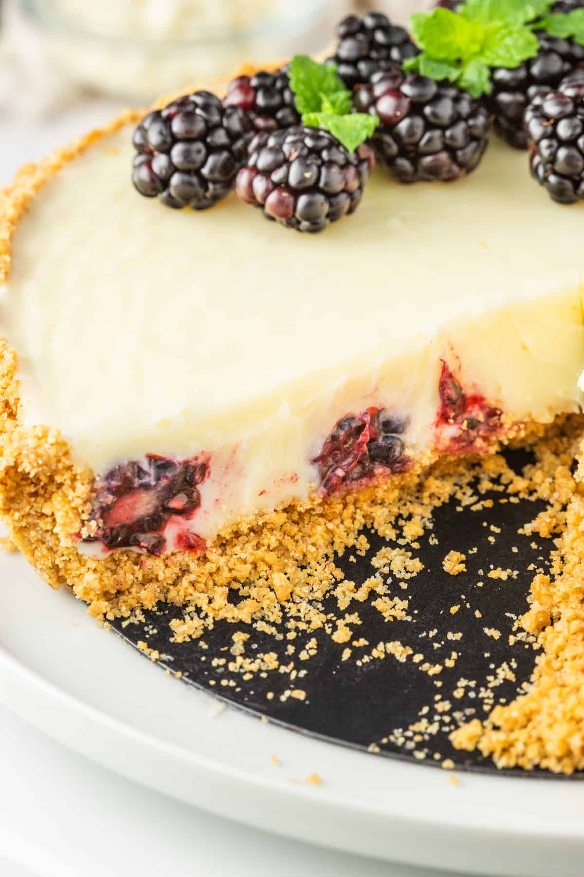 A white chocolate blackberry tart on a plate with a slice taken out.