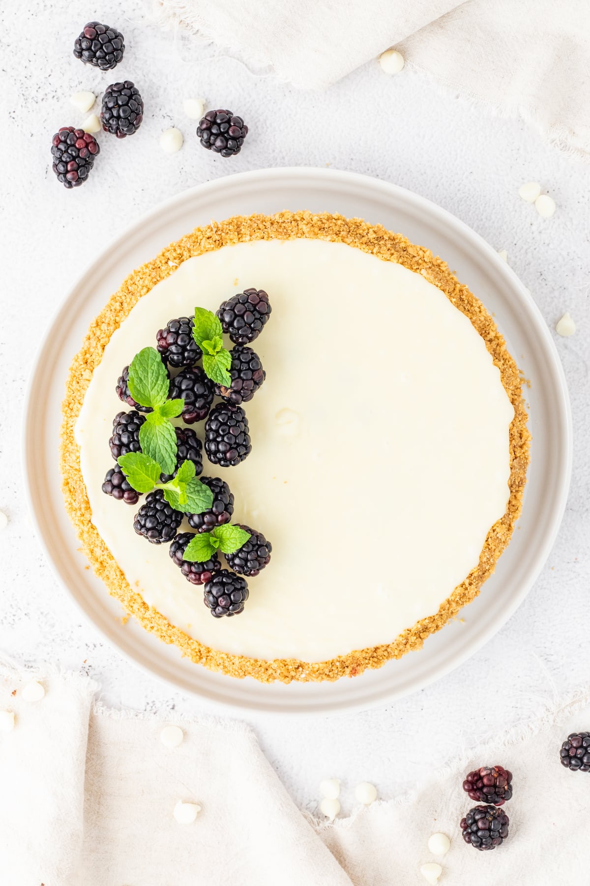 A heavenly white cheesecake adorned with plump blackberries and fresh mint leaves, elegantly presented on a pristine white plate.