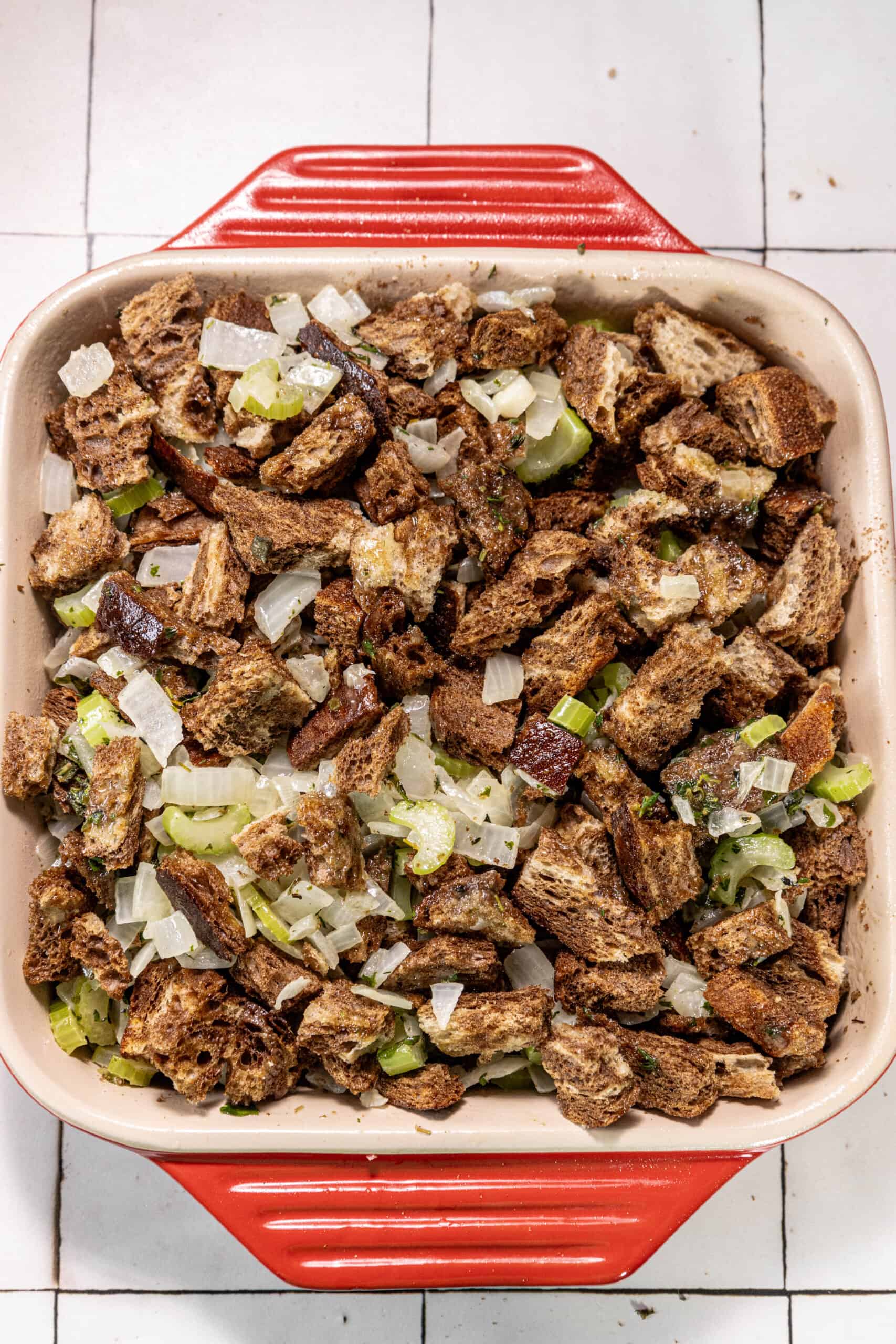 A red baking dish filled with bacon and vegetables.