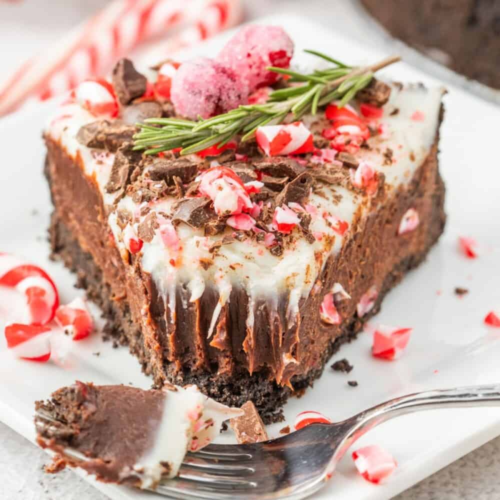 A slice of chocolate peppermint cheesecake with a candy cane garnish on a plate.