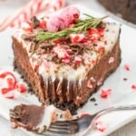 A slice of chocolate peppermint cheesecake with a candy cane garnish on a plate.
