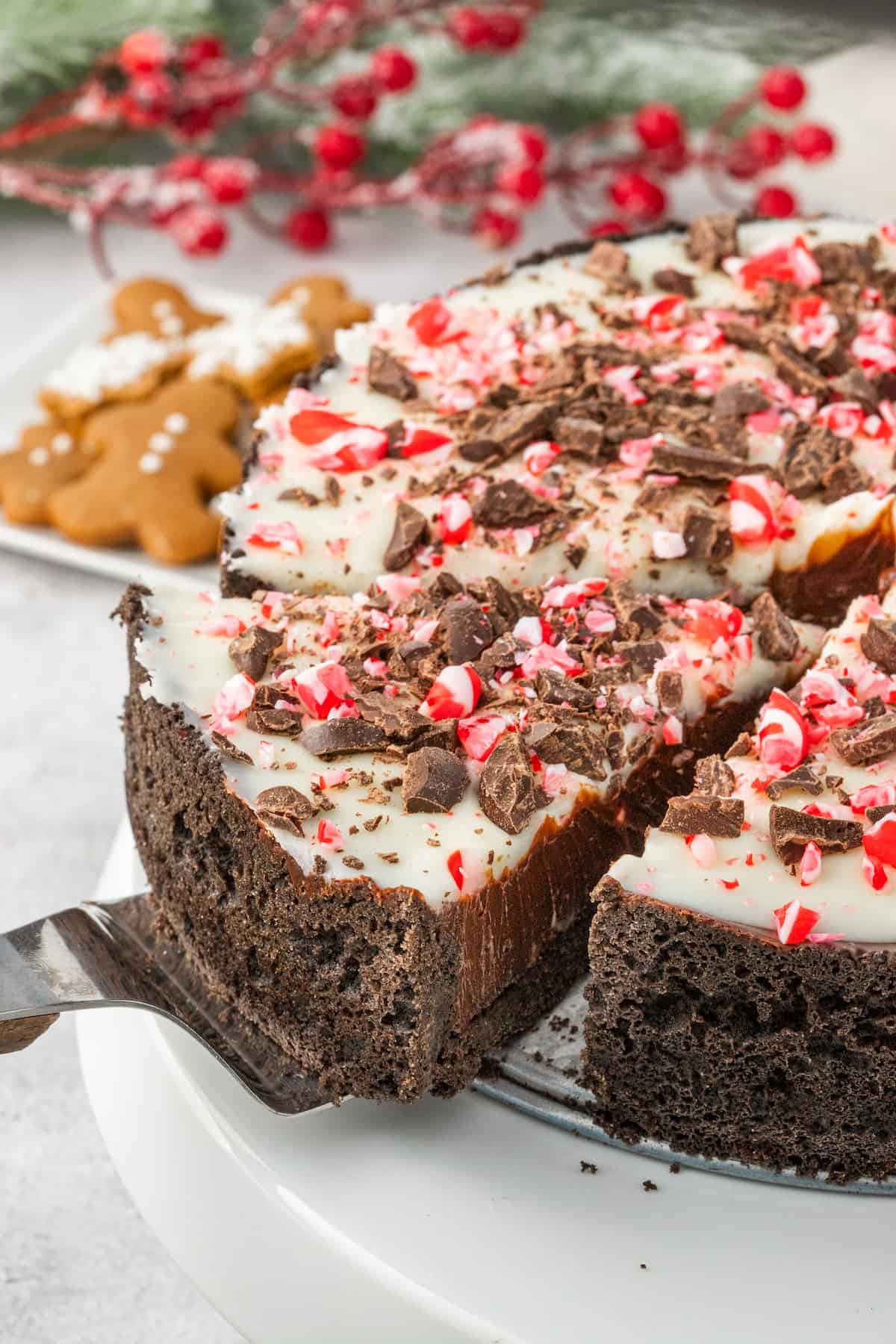 A chocolate peppermint cheesecake with a slice taken out, drizzled with rich chocolate ganache and topped with a festive candy cane.