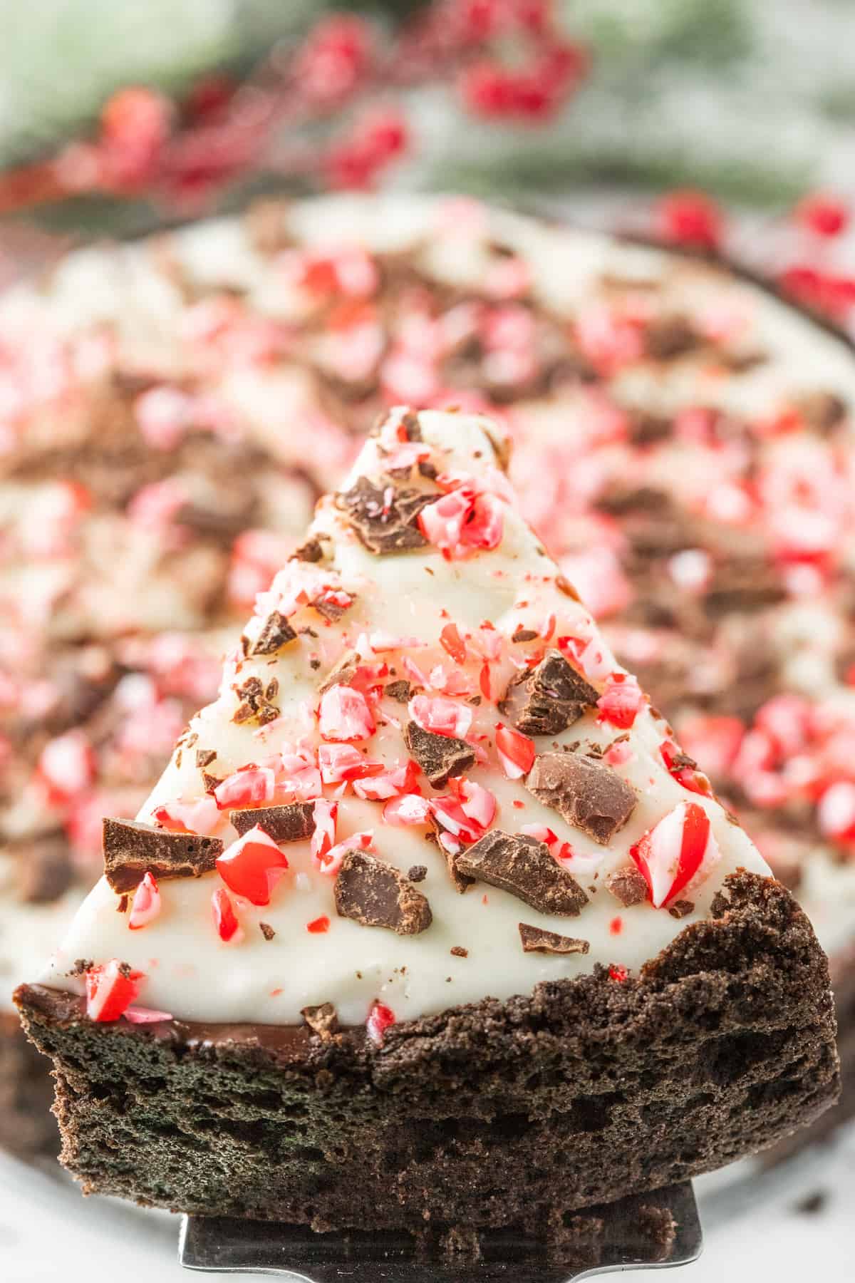 A slice of chocolate peppermint pie topped with a smooth chocolate ganache and a candy cane on a plate.