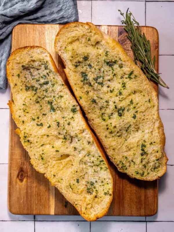 Two slices of bread on a cutting board with a sprig of rosemary.