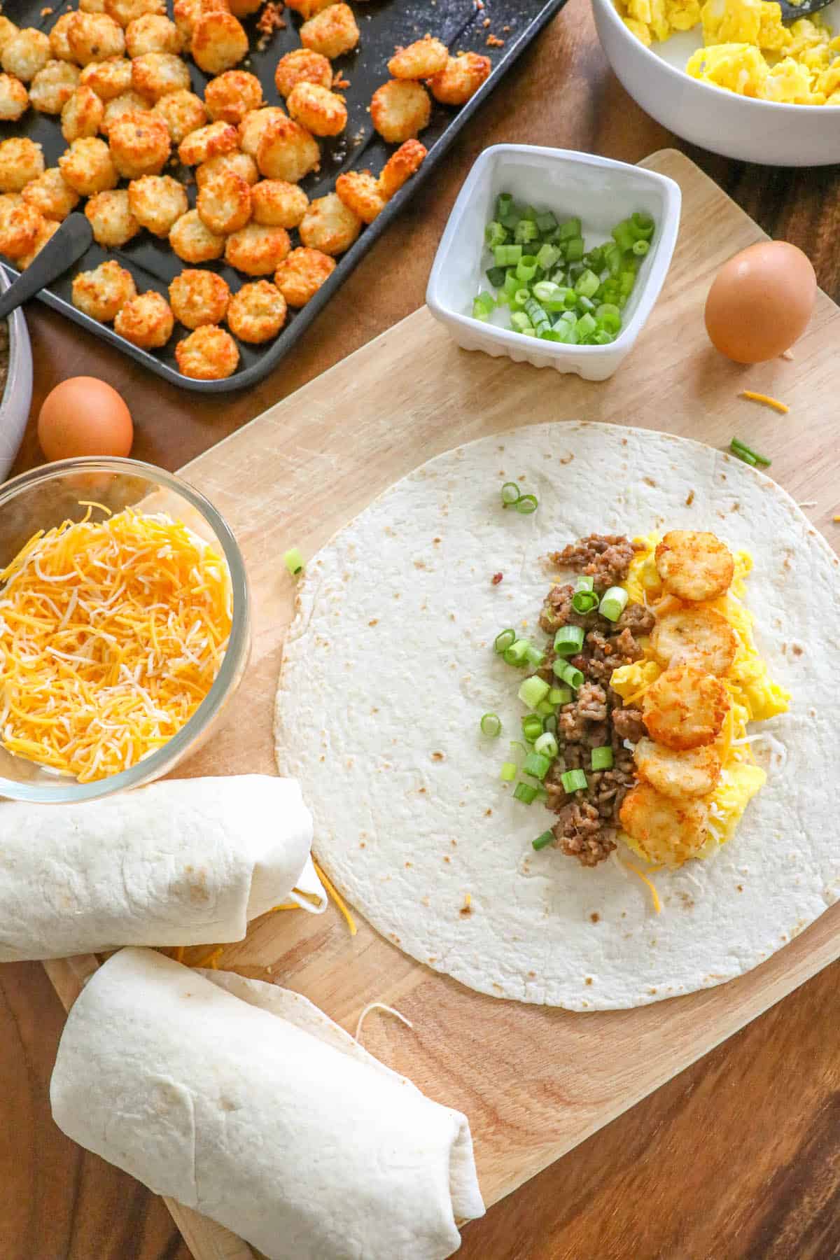 A wooden cutting board with various ingredients for freezer breakfast burritos on it.