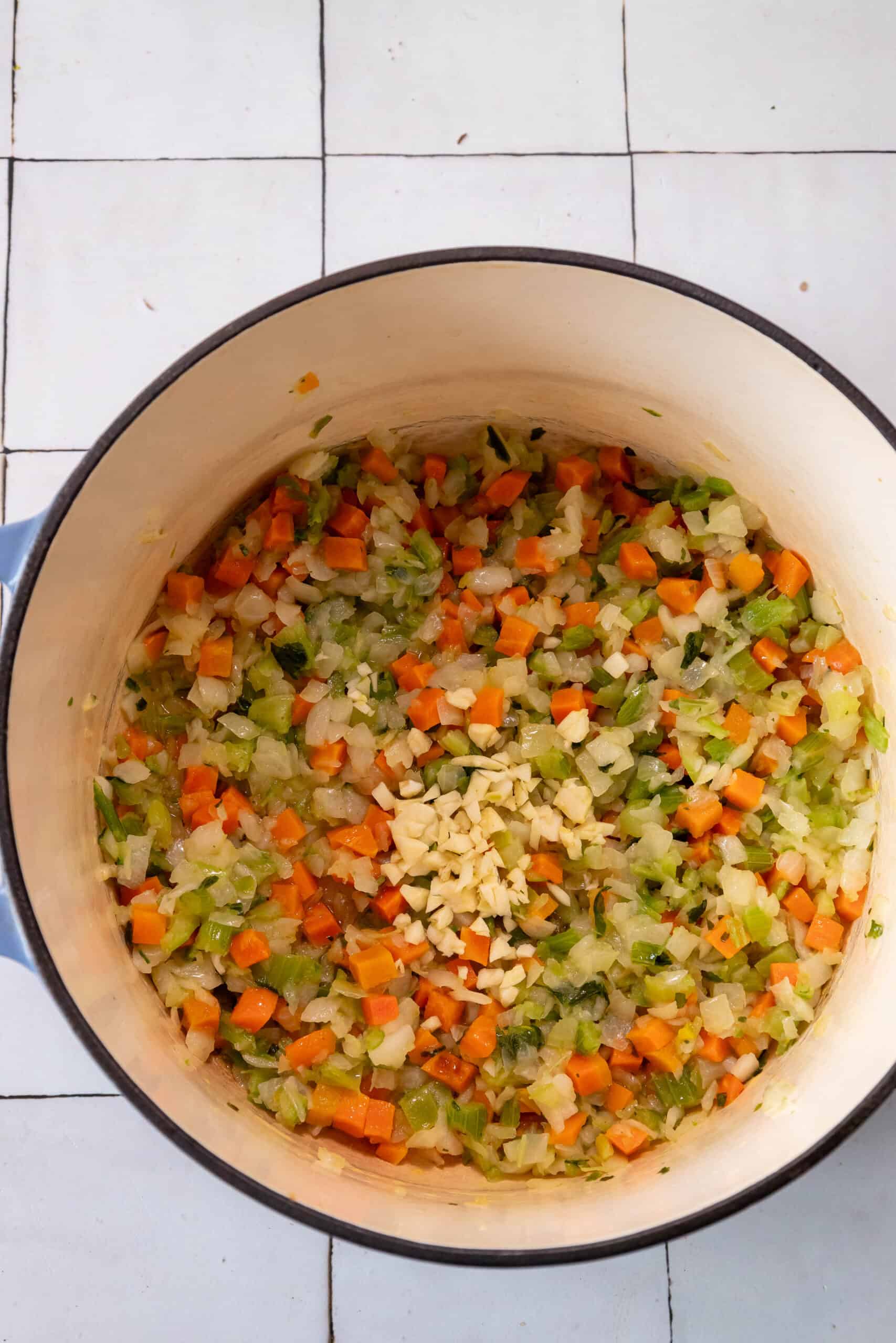 A pot filled with lemon chicken and tortellini soup on a tiled floor.