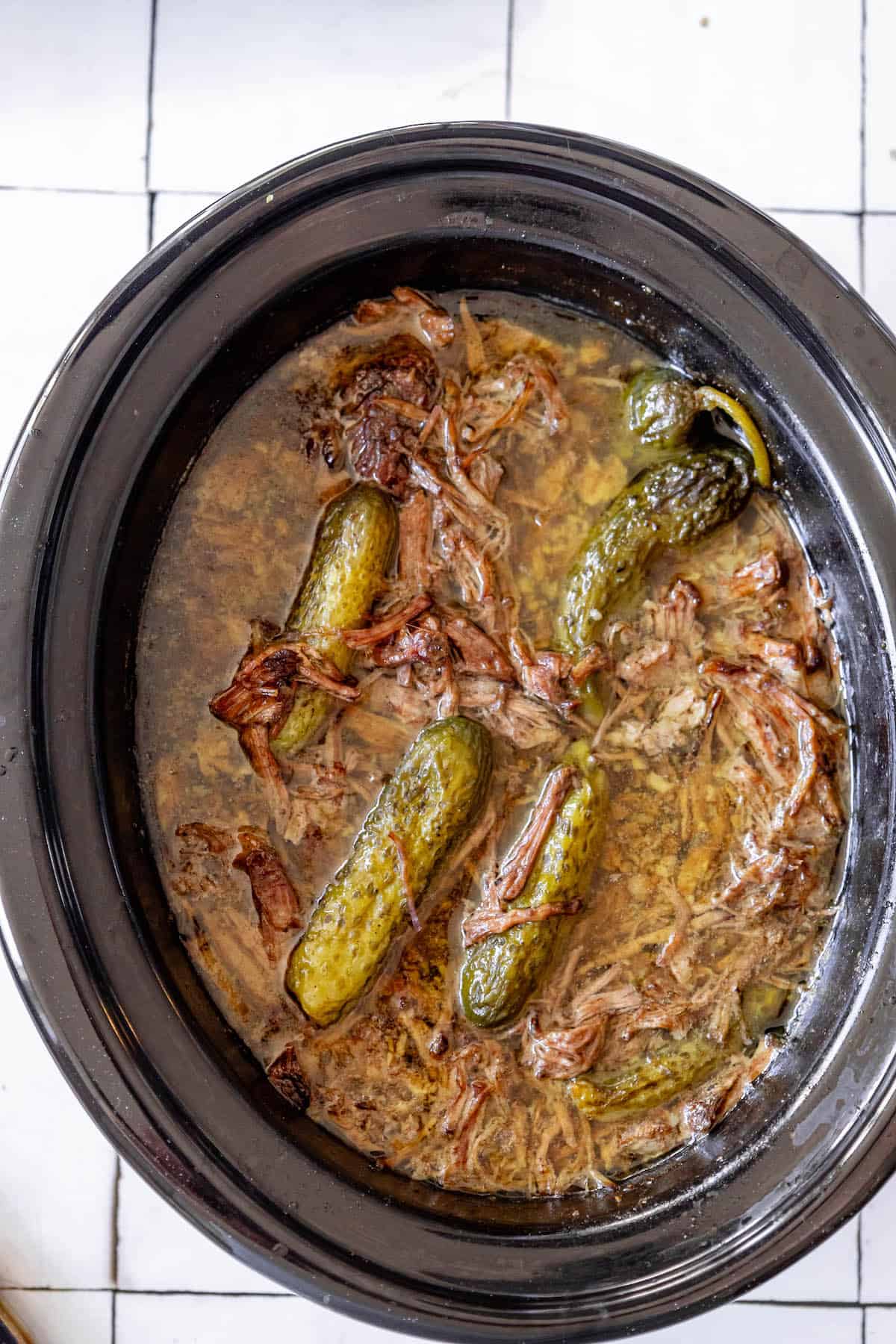 A crock pot full of Pot Roast cooked with pickles.
