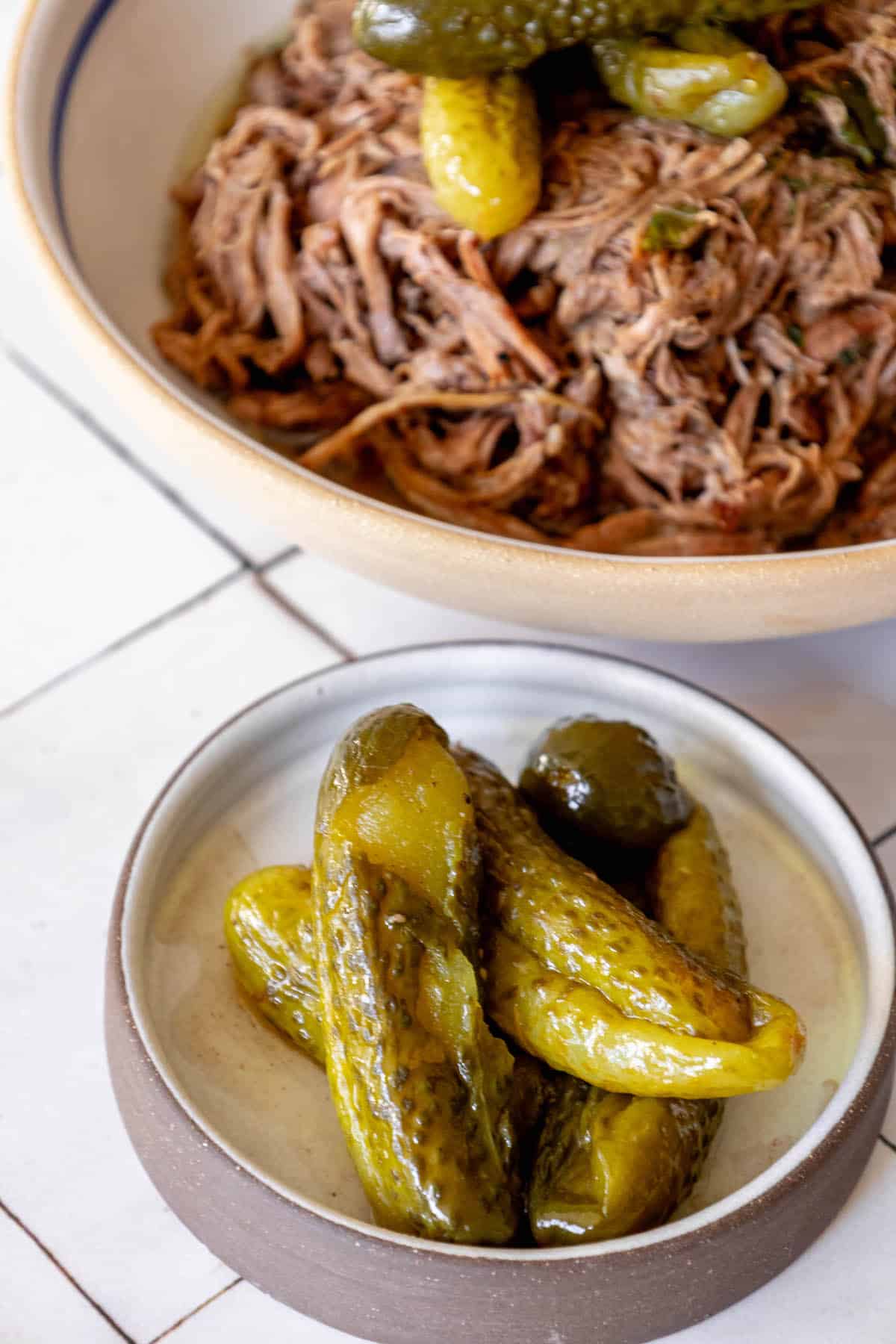 A bowl of pickles next to a serving of beef.