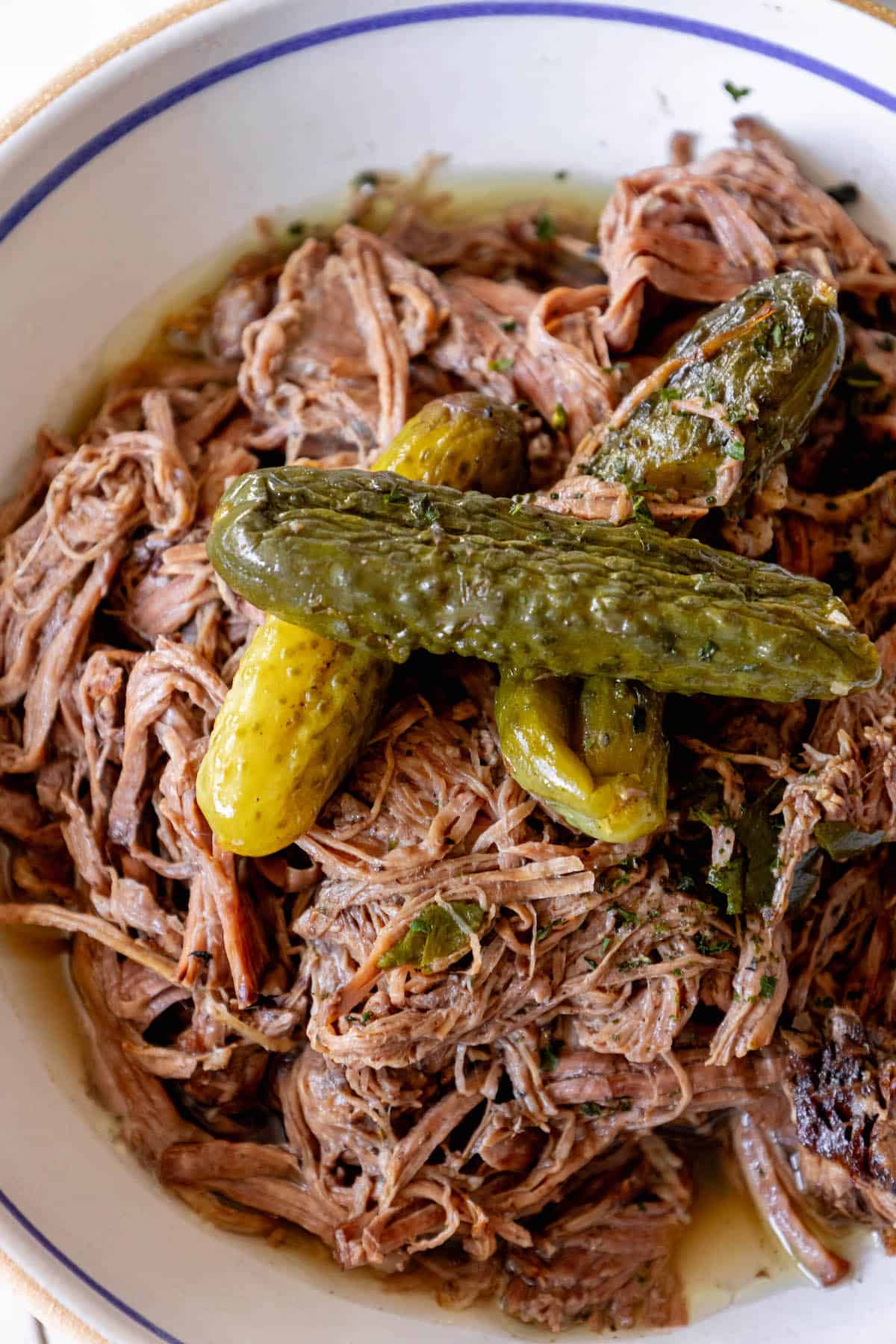 A bowl with pot roast and pickles in it.