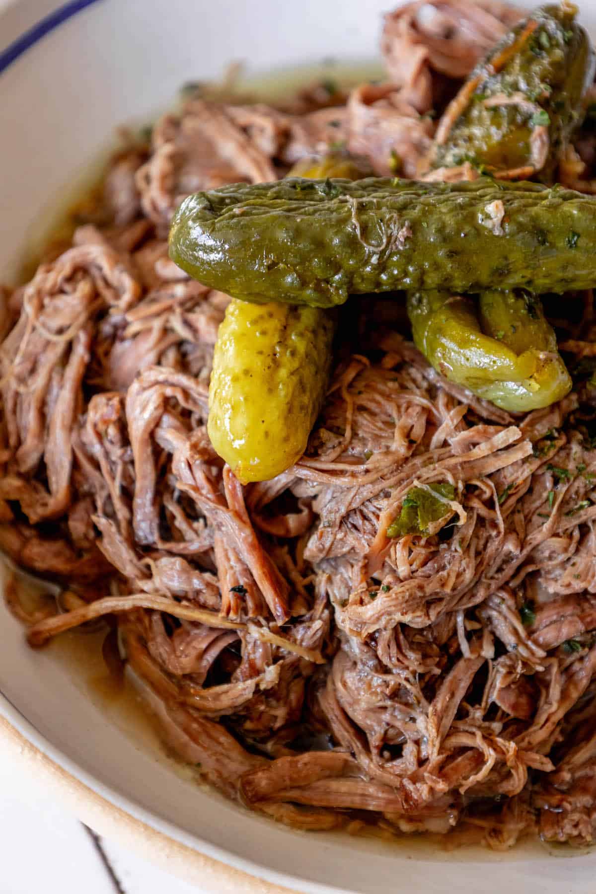 A bowl of pulled pork and pickles on a table.