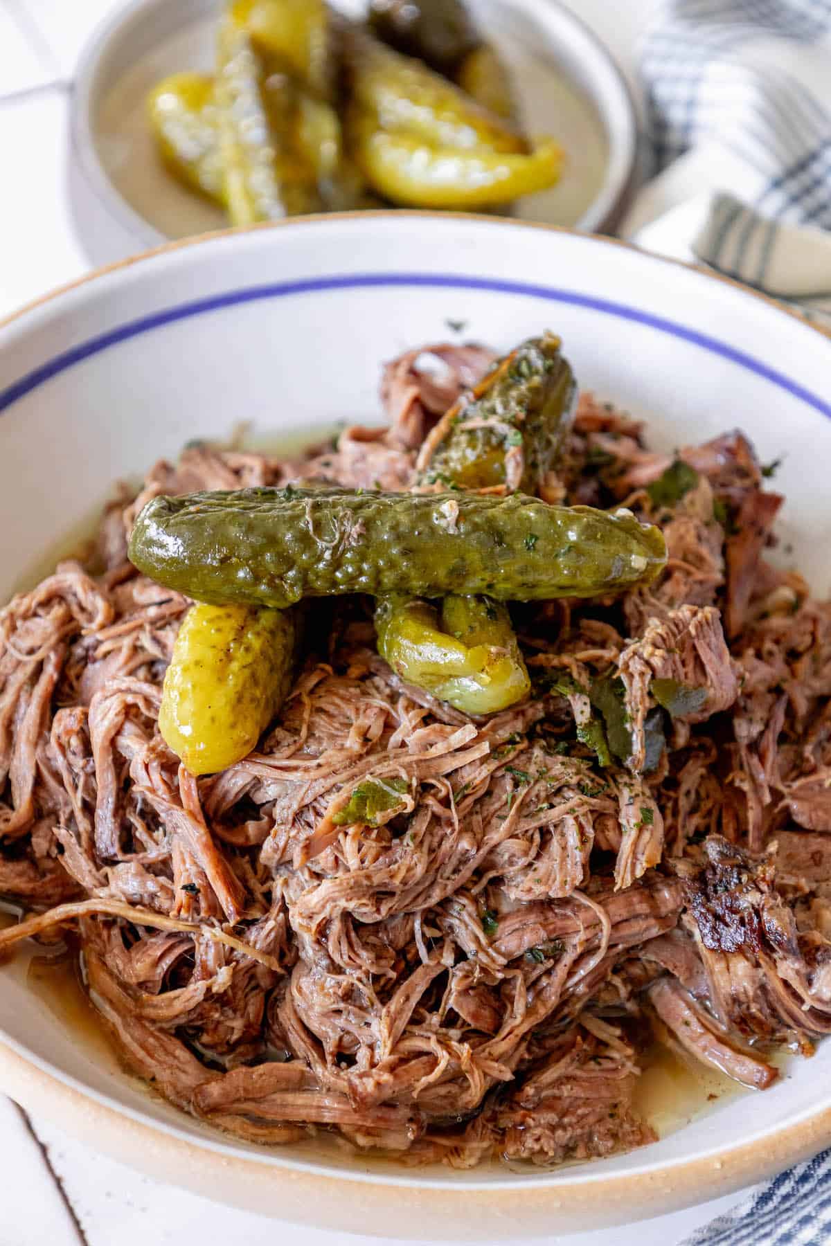 A bowl of pulled pork and pickles on a table with a side of Pickle Pot Roast.