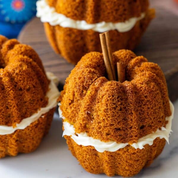 Mini Pumpkin Bread Mini Pumpkins with cream cheese frosting in the center, topped with cinnamon sticks, arranged on a surface—these resemble adorable pumpkin shaped pumpkin bread treats perfect for fall gatherings.