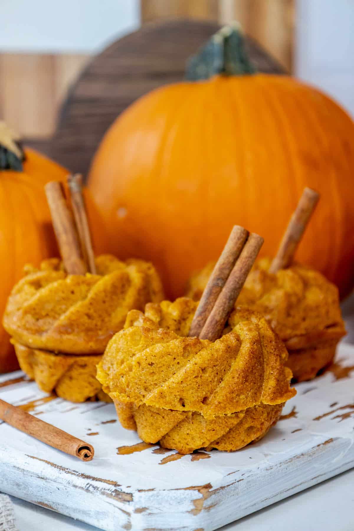 Pumpkin muffins with cinnamon sticks on a wooden cutting board, perfect for Halloween desserts.