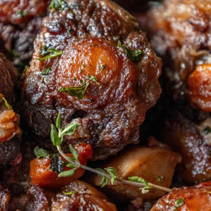 A close up of a delicious dish featuring roasted oxtail stew with potatoes and thyme.