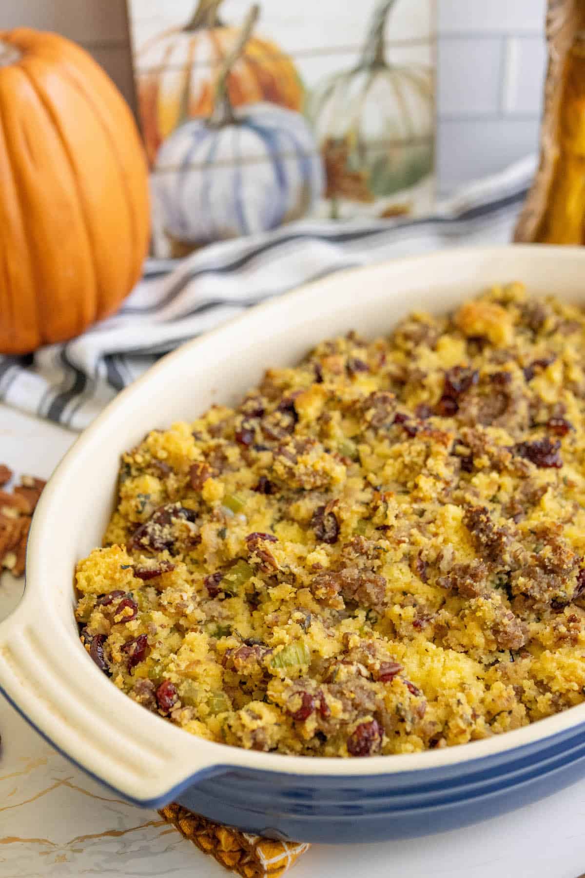 A dish of cornbread stuffing on a table with pumpkins and cranberries.