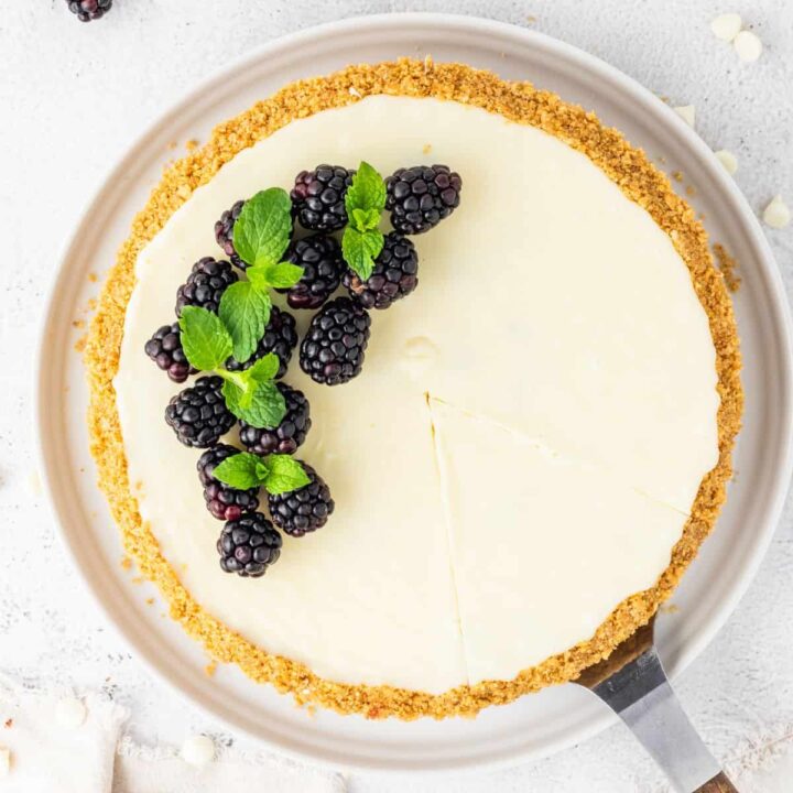 A slice of white chocolate blackberry tart with mint on a white plate.