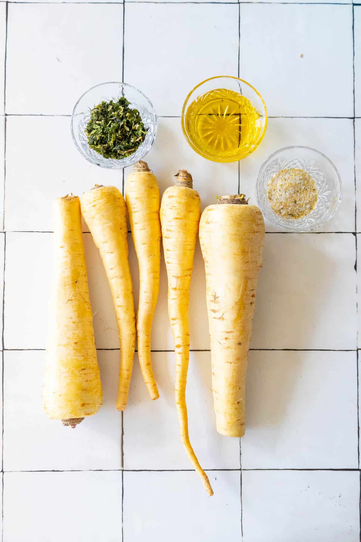 A group of roasted yellow carrots on a tiled floor.