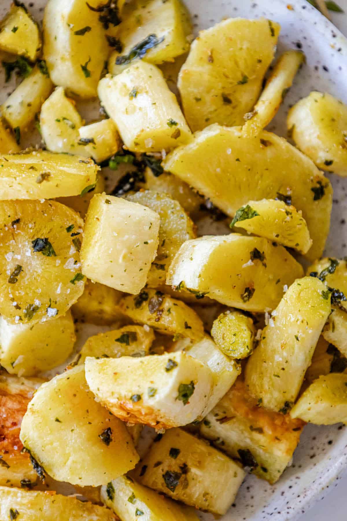 Roasted potatoes and parsnips on a plate with herbs.