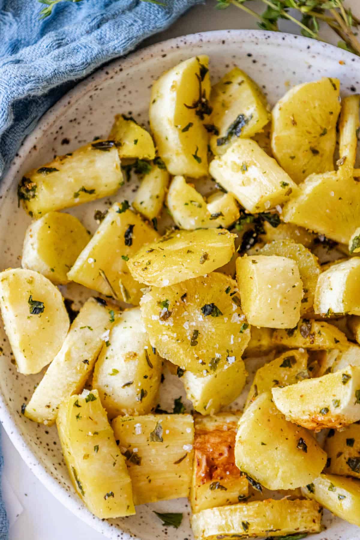 Roasted potatoes and parsnips in a white bowl with herbed thyme.
