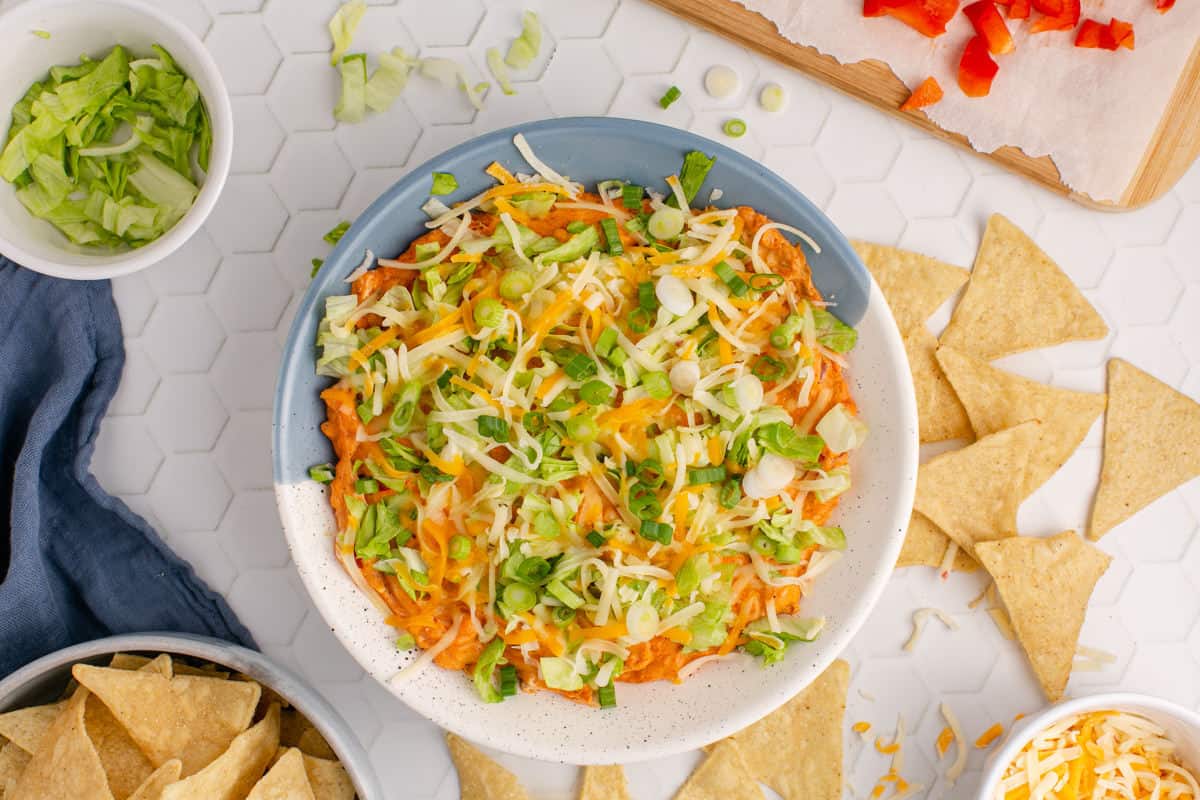 A bowl of hot taco dip with tortilla chips and shredded cheese.