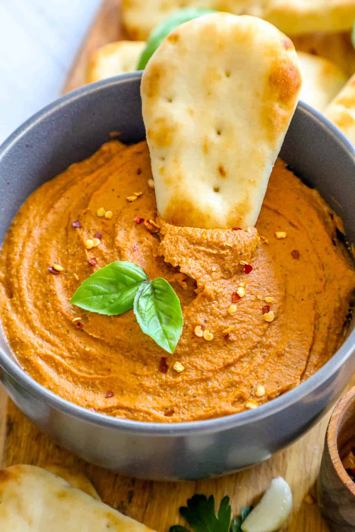 A bowl of hummus with pita chips on a wooden cutting board.