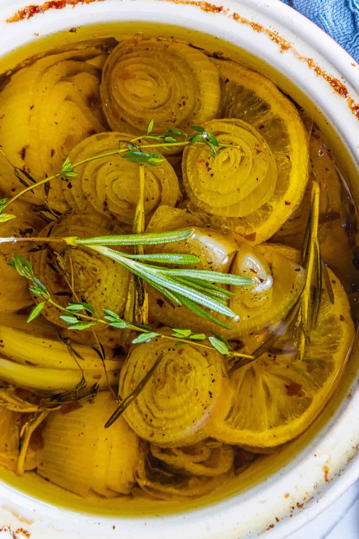 A bowl filled with shallots, onions, and sprigs of rosemary.