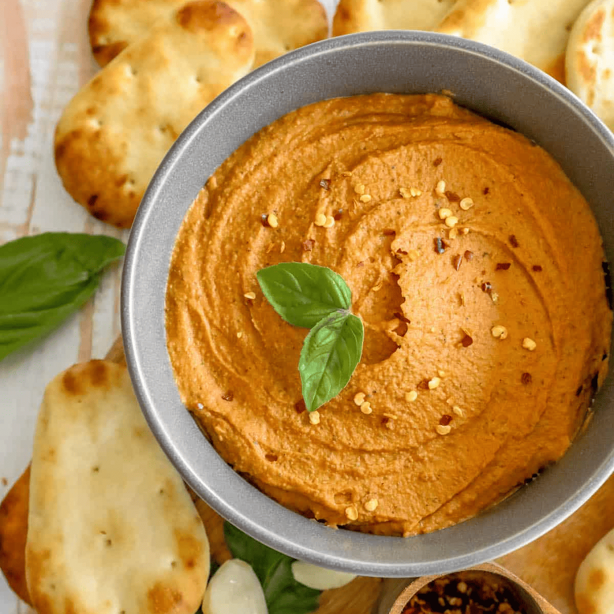 A delicious bowl of hummus layered with crackers and garnished with fragrant basil leaves.