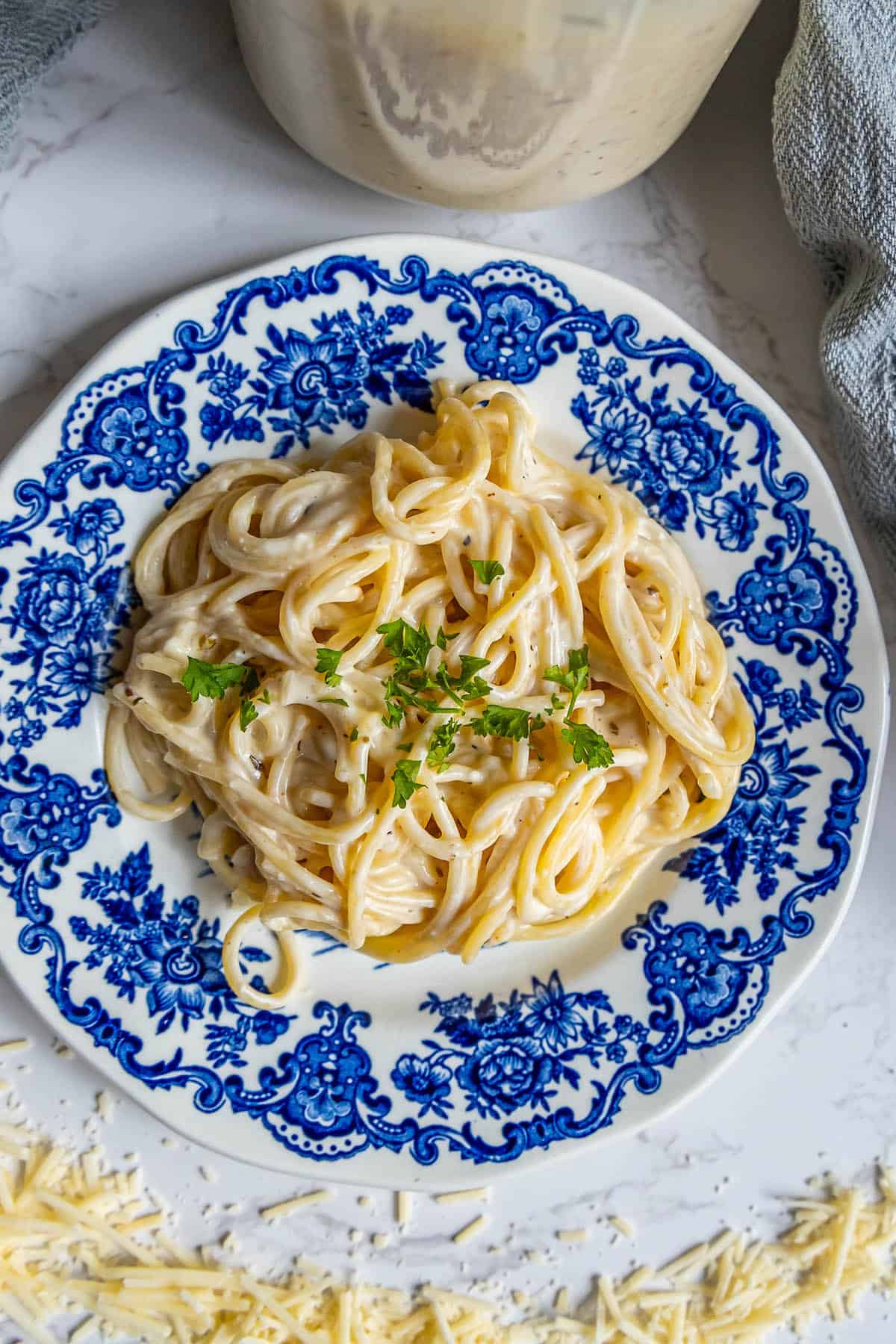 A blue and white plate with pasta topped with parmesan cheese.