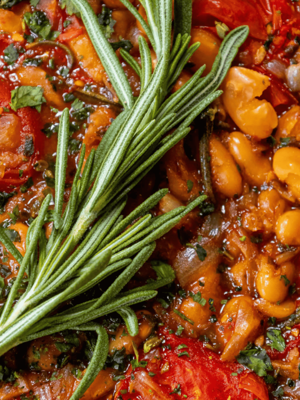 A brothy dish of herbed white beans with a sprig of rosemary.