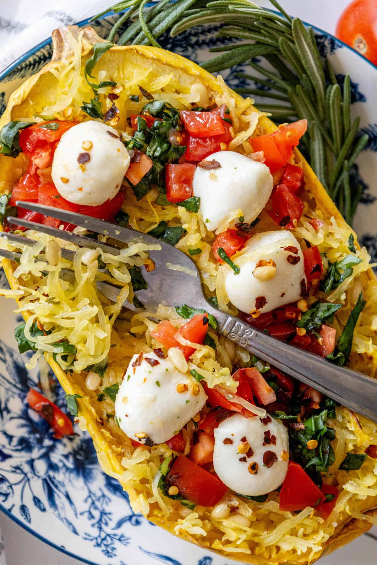 Baked Caprese spaghetti squash with mozzarella and tomatoes on a blue and white plate.