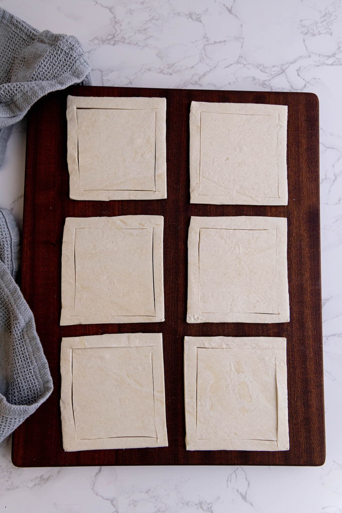 Four cranberry brie bites squares of dough on a cutting board.