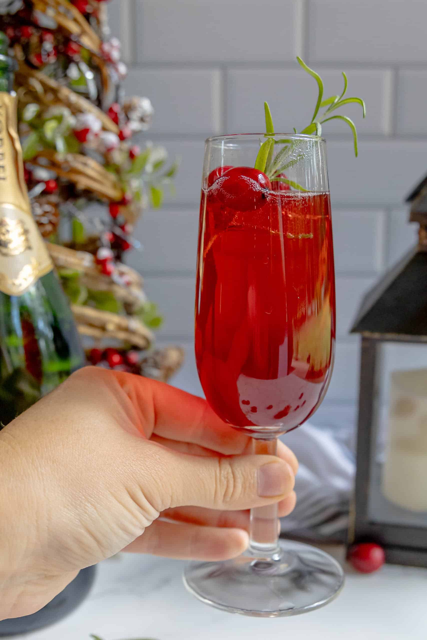 A hand holding a glass of cranberry champagne cocktail.