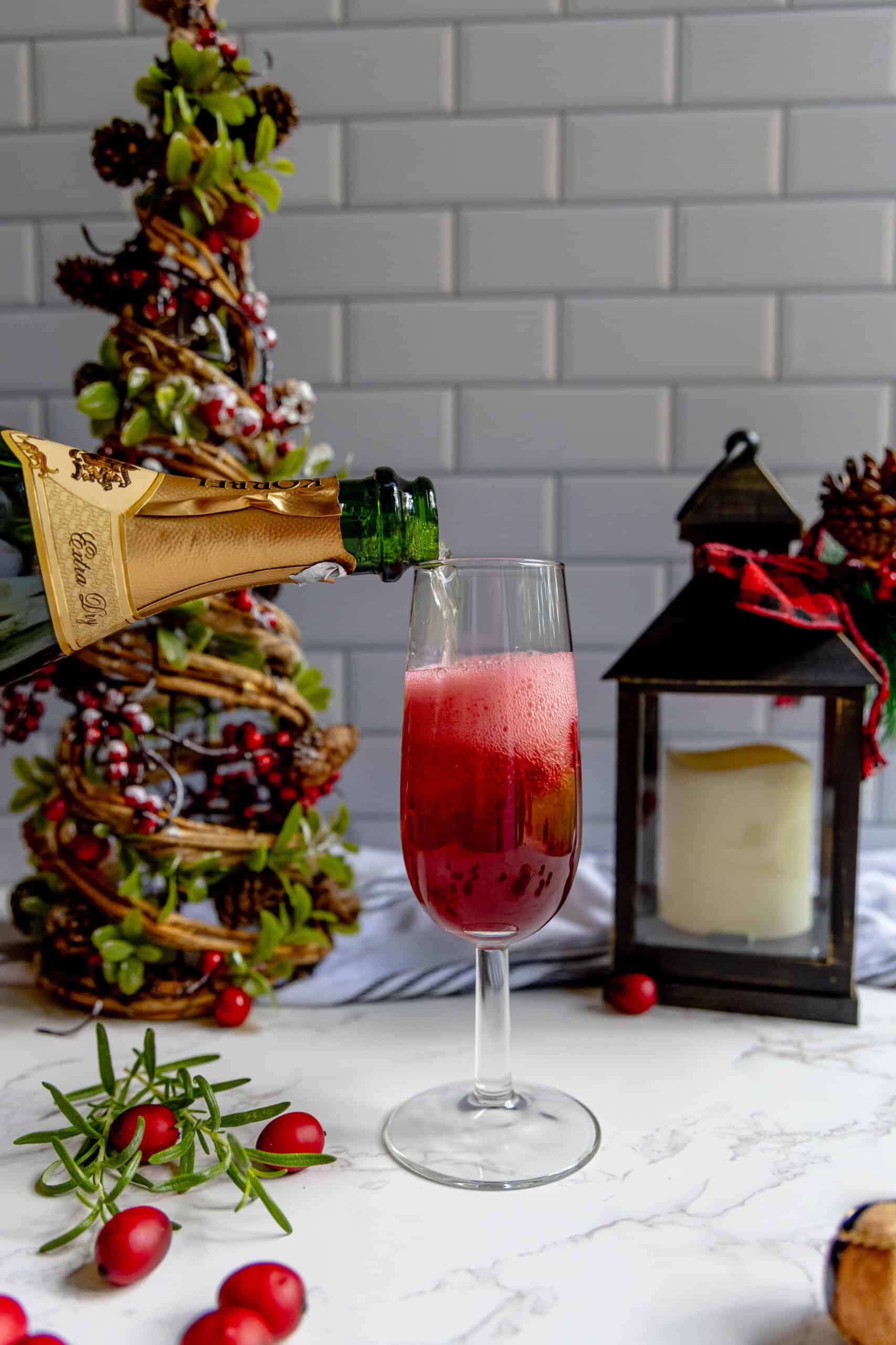 A bottle of champagne is being poured into a glass of cranberry juice, creating a refreshing cranberry champagne sparkler.