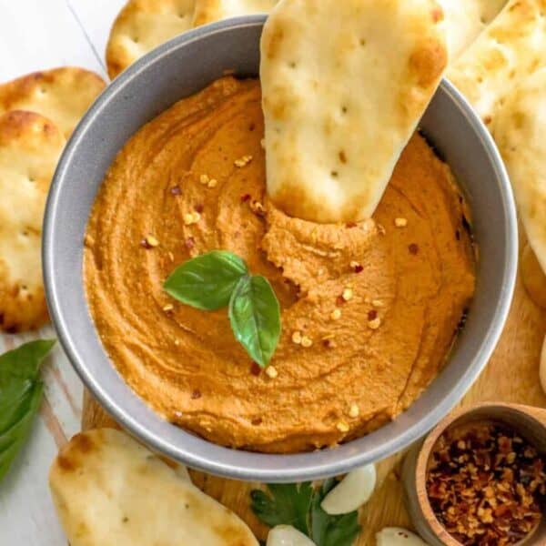 A bowl of hummus with crackers and garlic.