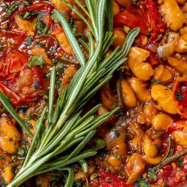 A dish of beans and tomatoes with a rosemary sprig.